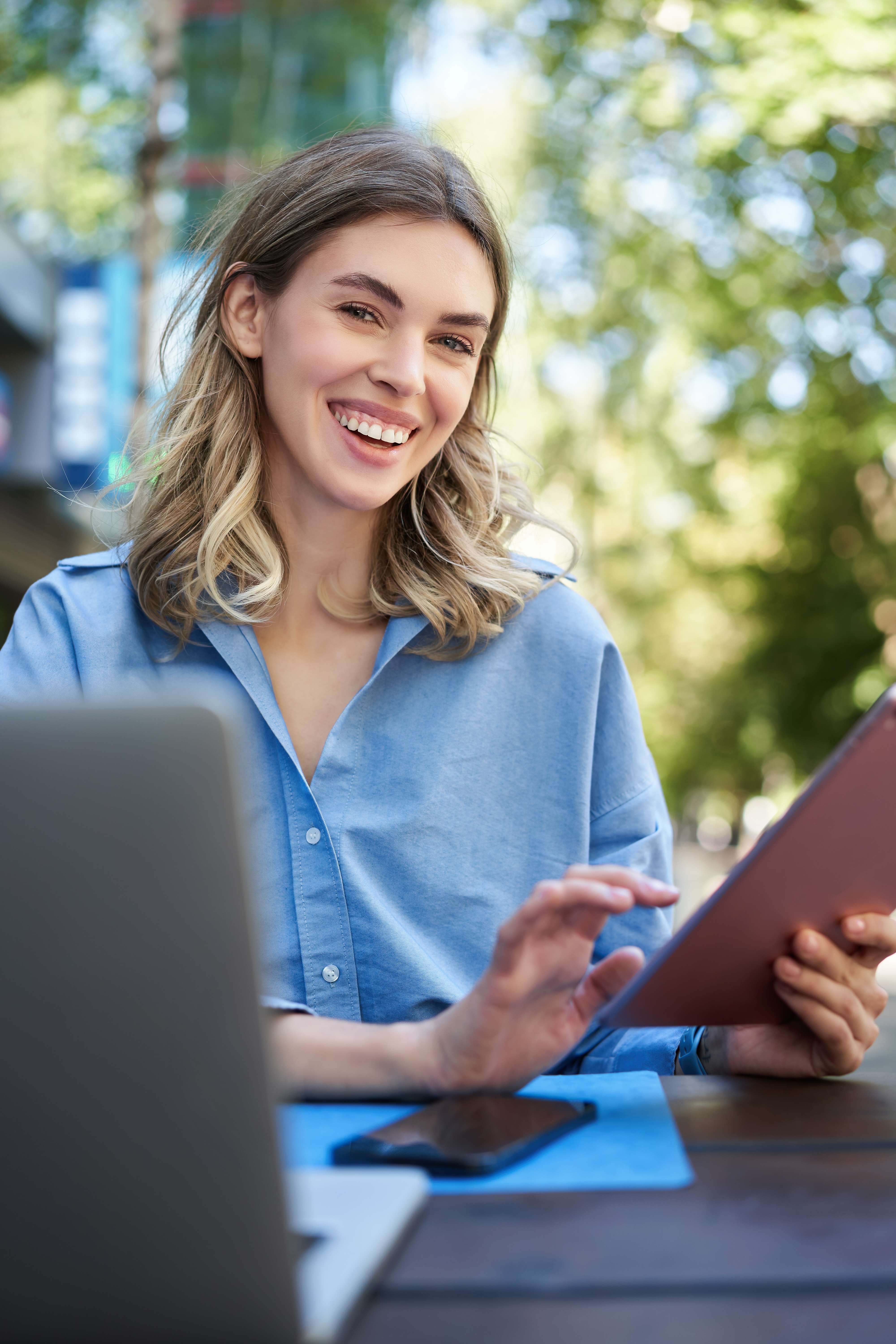 vertical-shot-smiling-successful-businesswoman-using-digital-tablet-sitting-outdoors-park-work (2)-1